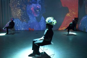 Persons wearing headwear made from spirals of upcycled plastic, surrounded by the film DEMO DAY projected in 360 degrees.  If possible, please load remote images to view the image.